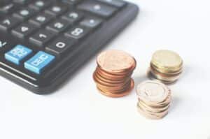 a black calculator with 3 piles of coins sat next to it