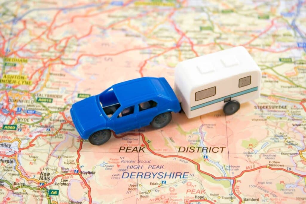 A blue toy car towing a white toy caravan sits on a map focused on the Peak District in Derbyshire, England—perfect for planning adventures and learning how to stay safe in your caravan.