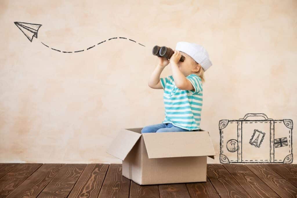 A child in a striped shirt and sailor hat sits in a cardboard box, looking through binoculars. A drawn paper aeroplane and suitcase decorate the background, highlighting imagination, adventure, and independent play.