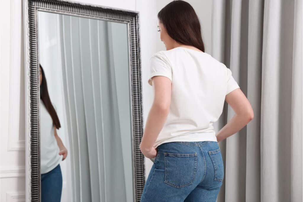 A woman in a white tshirt and jeans looking in the mirror