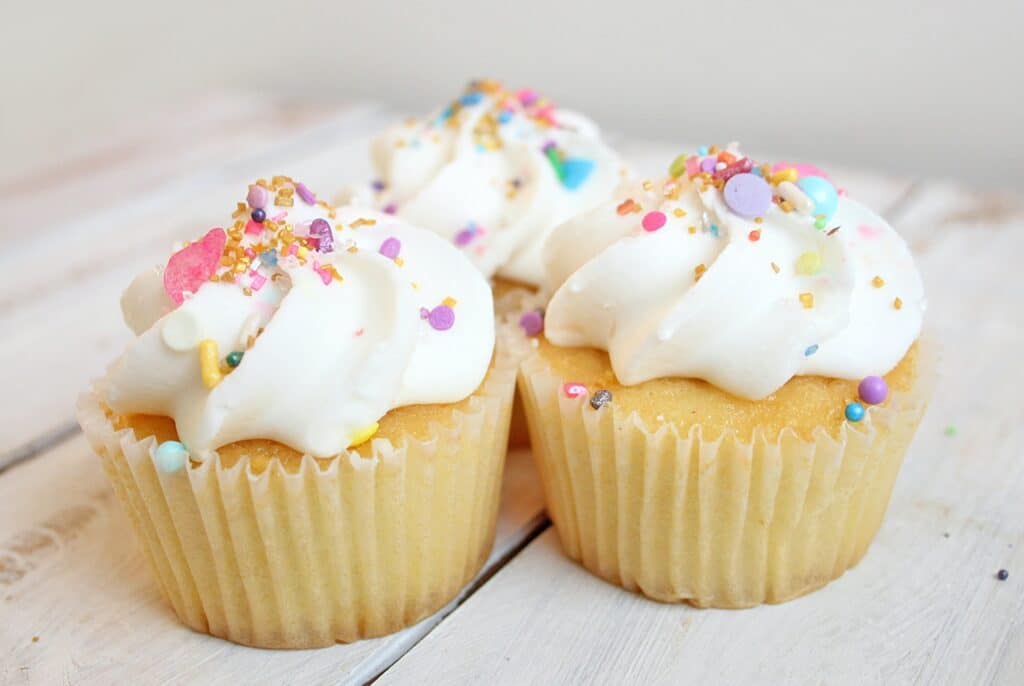 Three vanilla cupcakes decorated with white icing and colourful sprinkles