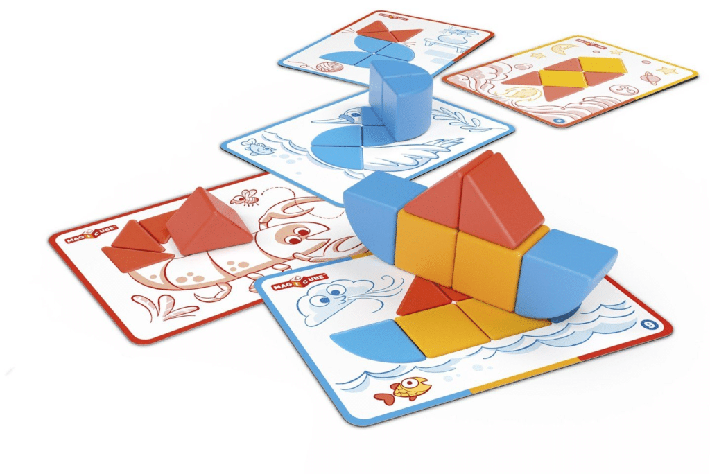Colourful geometric blocks are arranged on illustrated cards, forming shapes such as a fish, a boat, and a bird. The outlined cards guide block placement, encouraging independent play and creative exploration.