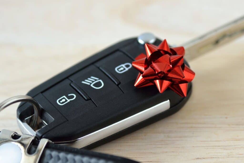 A close-up of a car key fob with buttons, decorated with a small red gift bow, resting on a light wooden surface—a subtle reminder of the Signs It’s Time To Change Your Vehicle.