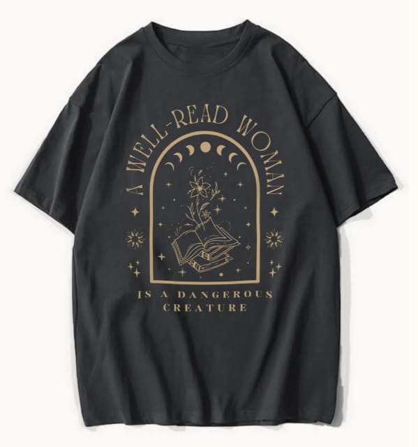 Black oversized top featuring a gold illustration of an open book with a blooming flower, stars, and moon phases. The text reads, "A well-read woman is a dangerous creature.