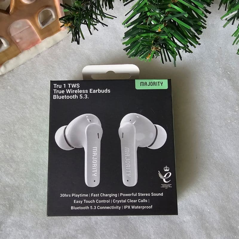 A box of Majority Tru 1 TWS True Wireless Earbuds sits on a grey surface beside a Christmas tree branch and decorative house, highlighting Bluetooth 5.3, 30hrs playtime, and waterproof design—perfect for a festive Christmas present.