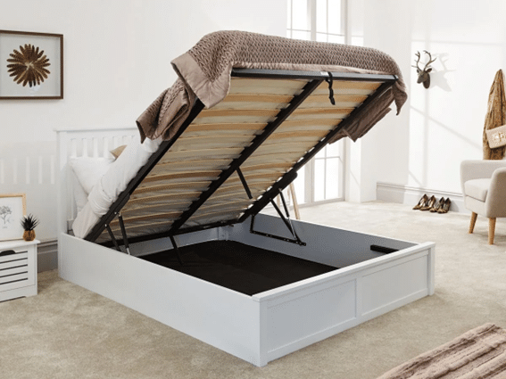 A white ottoman bed stands in a bright, modern bedroom with neutral decor and light carpet, its mattress lifted to reveal spacious storage underneath—perfect for keeping your room tidy and organised.