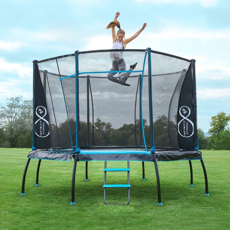 A woman energetically jumps on a trampoline with safety netting in a grassy outdoor area, her arms raised and hair flying—a playful scene that highlights the joy and benefits of childhood development amid trees and blue sky.