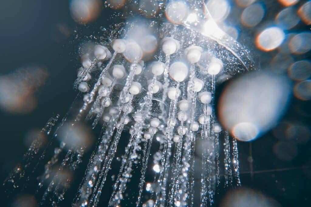 Close-up view of water droplets streaming from a steam showerhead, with light reflecting off the beads of water, creating a sparkling, abstract effect.