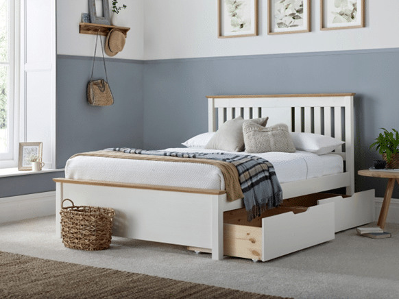 A modern bedroom with a white and wood bed frame featuring storage drawers, a basket on the floor, grey and white walls, framed art, and neutral bedding with pillows and a checked throw.
