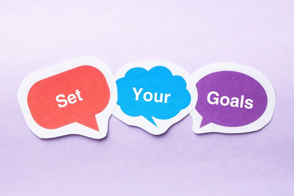 Three colourful speech bubbles on a light purple background with the words “Set” (red bubble), “Your” (blue bubble), and “Goals” (purple bubble), encouraging you to focus on your academic goals.