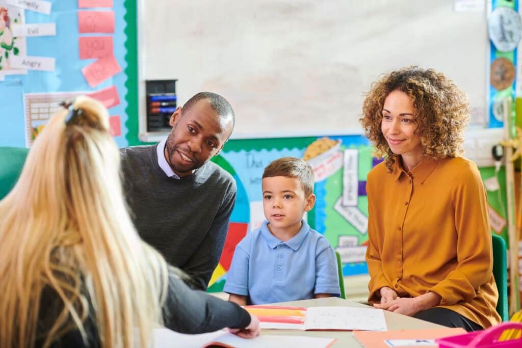 a parents evening consultation between a teacher, two parents and their child in a classroom