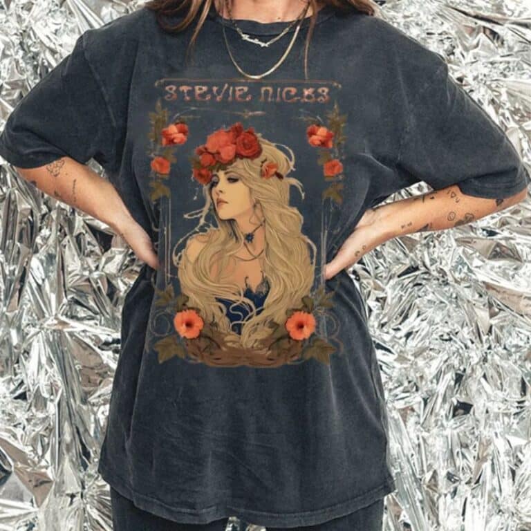 A person wearing an oversized black T-shirt featuring an illustrated portrait of a woman with long blonde hair, a floral crown, and the text "Stevie Nicks." The metallic background adds a shiny, modern touch.