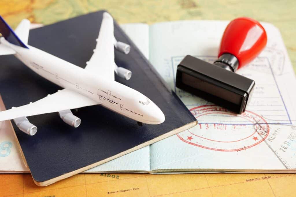 A model aeroplane, a passport, and a rubber stamp rest on an open passport displaying several entry and exit stamps, all placed on a world map background—perfect for envisaging your next travel job adventure.