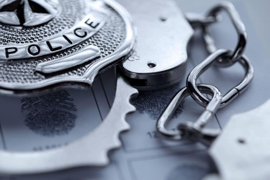 A close-up of a police badge and metal handcuffs lying on a fingerprint card, suggesting police work and criminal investigation themes.