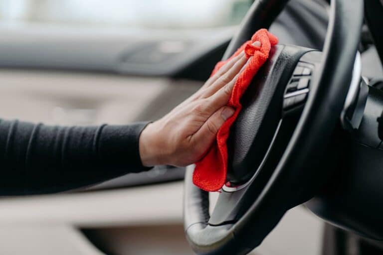 A person wipes a car’s steering wheel with a red cloth, making sure the interior stays spotless and the car looks fresh.