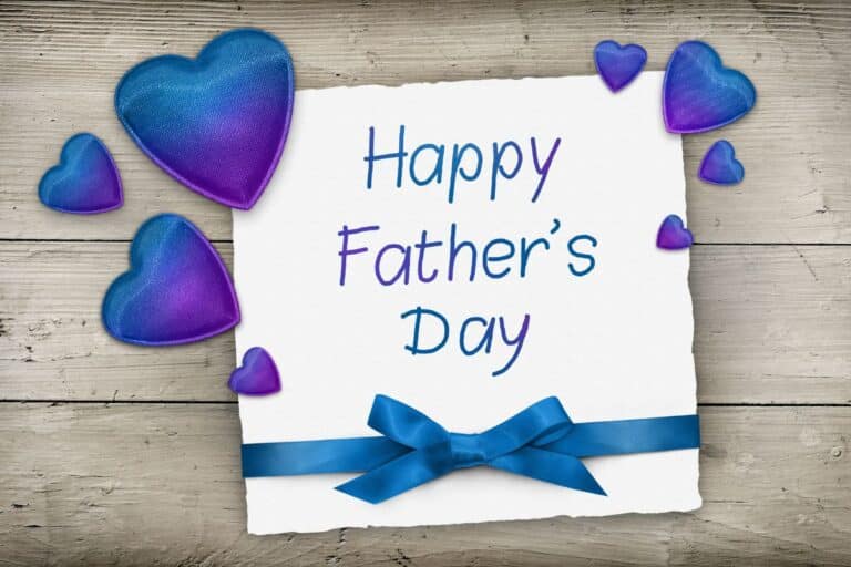 A white card with "Happy Father's Day" written in blue, decorated with a blue ribbon bow—perfect for cotton traders—and surrounded by blue and purple gradient hearts on a wooden background.