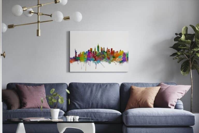 A modern living room with a blue sofa, pink and brown cushions, a glass coffee table with a plant, a potted plant in the corner, and striking cityscape wall art above the sofa.
