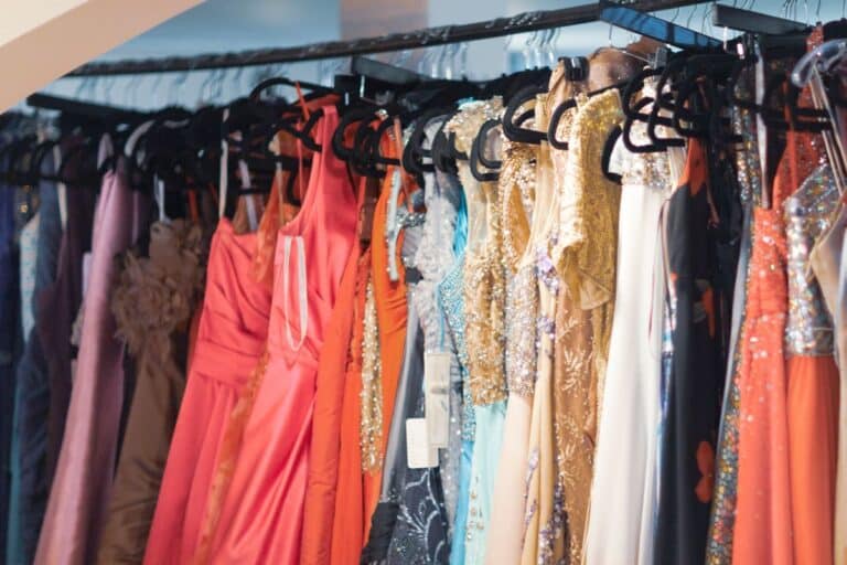 A row of elegant formal and cocktail dresses in various colours and styles hangs on black hangers in a boutique or shop.