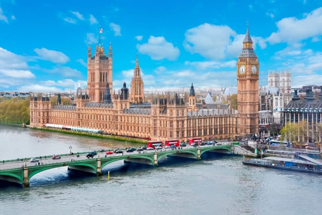 A view of the Palace of Westminster and Big Ben in London, with the River Thames and Westminster Bridge in the foreground—an iconic sight often enjoyed on city-based school trips—under a bright blue sky with scattered clouds.