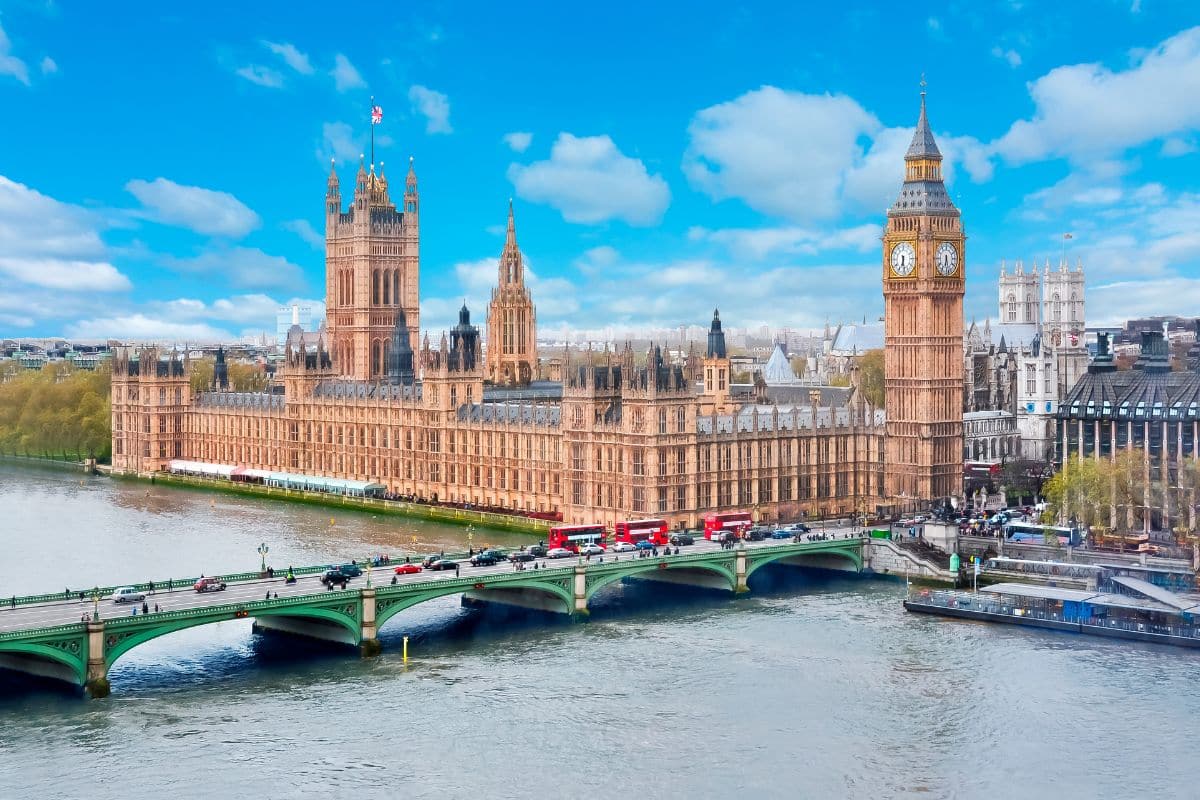 A view of the Palace of Westminster and Big Ben in London, with the River Thames and Westminster Bridge in the foreground—an iconic sight often enjoyed on city-based school trips—under a bright blue sky with scattered clouds.