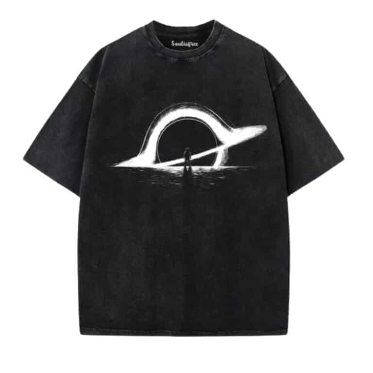 An artistic clothing piece: this black oversized T-shirt features a white ringed planet or halo above a reflective surface, with a small silhouette of a person standing beneath the ring at the design’s centre.