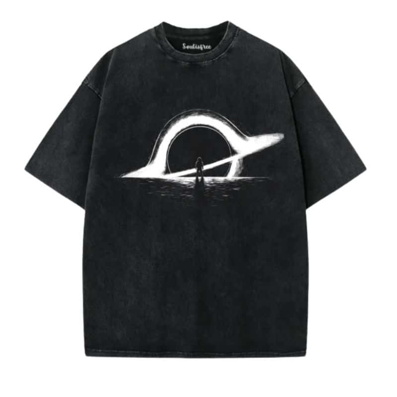 An artistic clothing piece: this black oversized T-shirt features a white ringed planet or halo above a reflective surface, with a small silhouette of a person standing beneath the ring at the design’s centre.