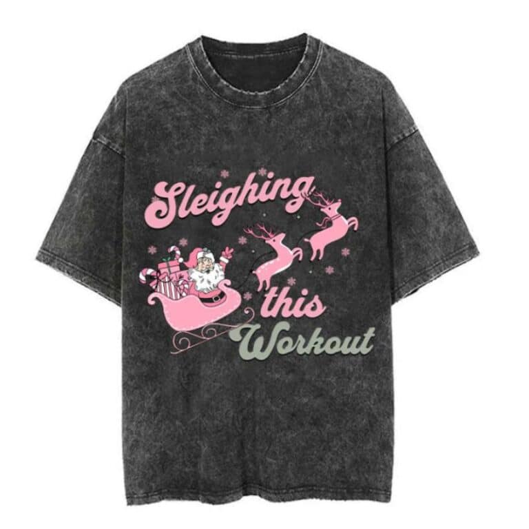 A black, acid-wash gym wear T-shirt features a pink design of Father Christmas in a sleigh pulled by two reindeer, with the words "Sleighing this Workout" in pink and green text.
