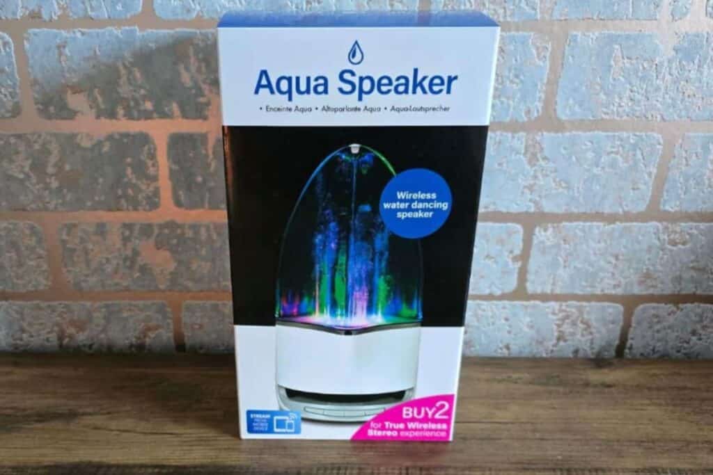 A boxed Aqua Bluetooth Speaker rests on a wooden surface, showcasing a clear dome with colourful LED lights. The packaging features "wireless water dancing speaker" and a "BUY 2 for true wireless stereo experience" offer.