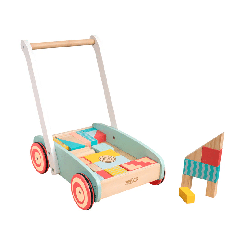 A colourful wooden baby walker with red wheels, filled with multicoloured wooden blocks. Some blocks and toys are stacked into a small structure beside the walker.