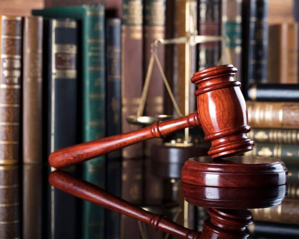 A wooden judge’s gavel rests on a sound block, with law books and a brass scales of justice in the background, capturing the essence of law, justice, and a dedicated lawyer’s pursuit of fairness.