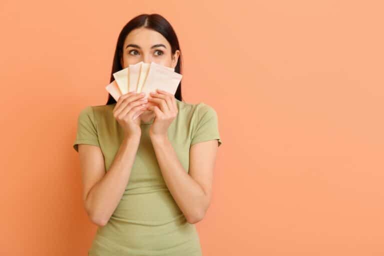A woman in a green shirt holds four sanitary towels in front of her face, symbolising menstruation awareness, as she looks to the side against an orange background.