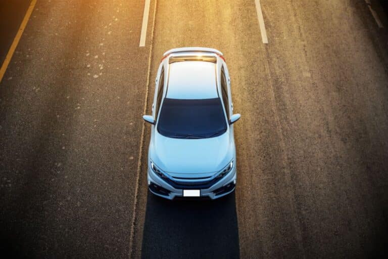 A white saloon, owned by motorists who value tranquillity, is parked in the middle of an empty, sunlit road. The road markings and warm light create a calm, open atmosphere.