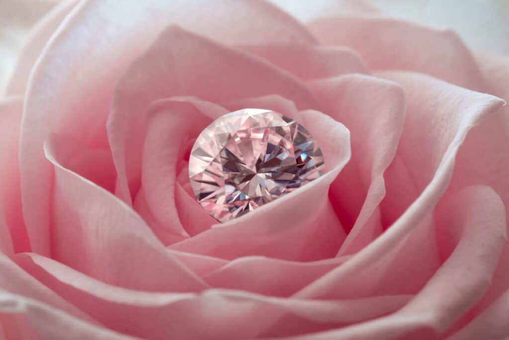 A sparkling lab-grown diamond rests at the centre of a soft pink rose, nestled among delicate petals.