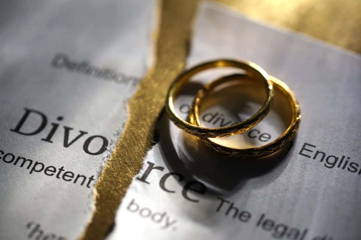 Two gold wedding rings rest on a torn piece of paper with the word “Divorce” visible, symbolising the end of a marriage or relationship, often seen in cases of grey divorce.