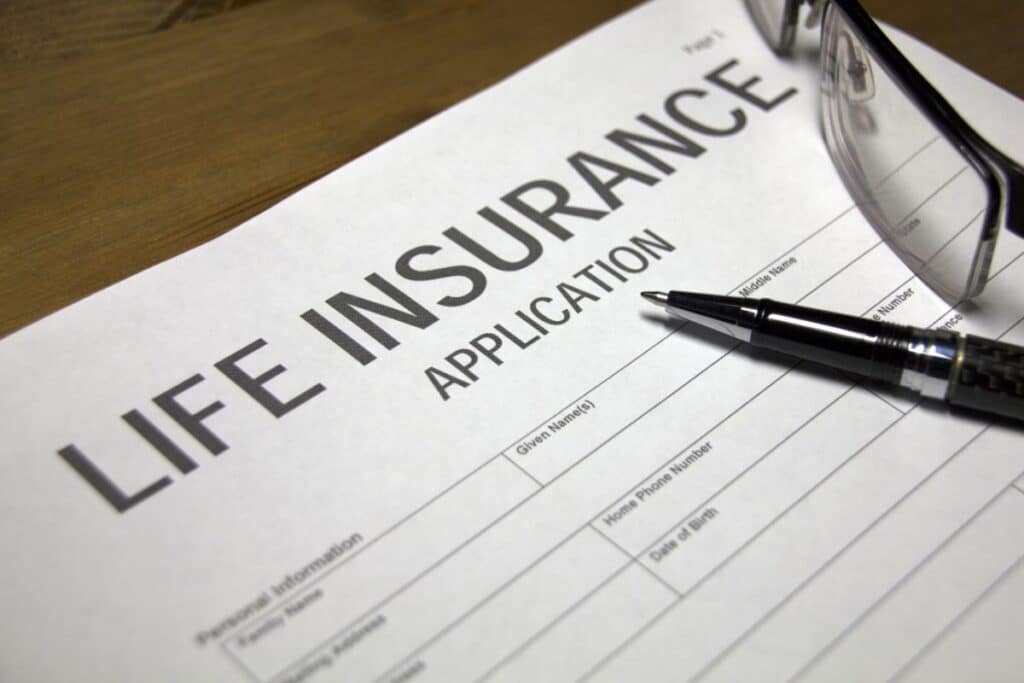 A close-up of a life assurance application form on a wooden table, with a pen placed on top and a pair of spectacles resting nearby, highlighting the importance of careful consideration when applying for life assurance.