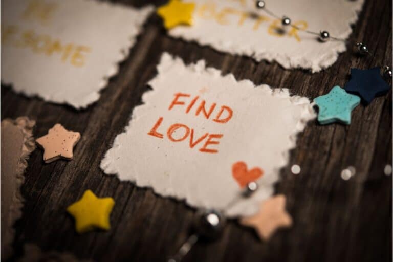 A piece of textured paper with uneven edges reads "FIND LOVE" in red letters, surrounded by small star-shaped decorations and a string of silver beads—a gentle reminder that dating as a parent can be magical, too.