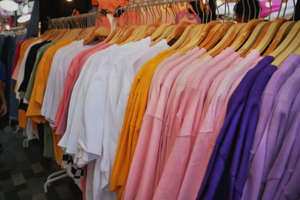 A row of colourful baby tees, including white, yellow, pink, and purple, hang neatly on wooden hangers on a clothes rail in a shop.