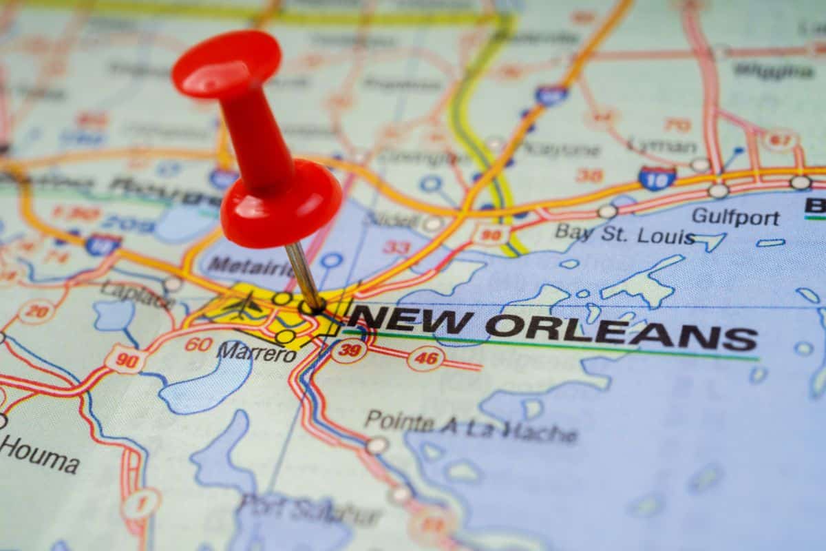 A red drawing pin marks the location of New Orleans on a detailed road map, with nearby cities and motorways visible around the highlighted area.