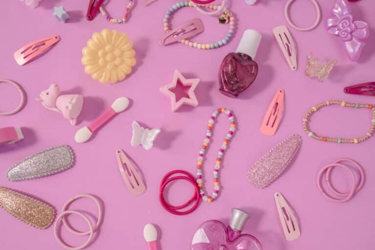 Various pink and pastel-coloured hair clips, jewellery, hair ties, and decorative accessories are scattered on a pink background—perfect for everyday wear or adding fun Y2K fashion style with barrettes, beaded bracelets, nail varnish, and cute butterfly shapes.