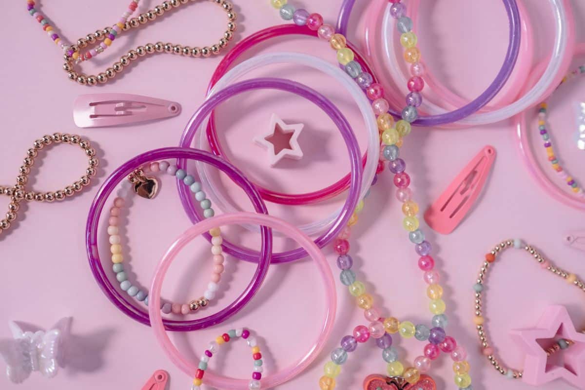 Colourful plastic bangles, beaded bracelets, pastel hair clips, a star-shaped ring, and a butterfly charm—perfect for adding Y2K style to your wardrobe—are arranged on a pink background.